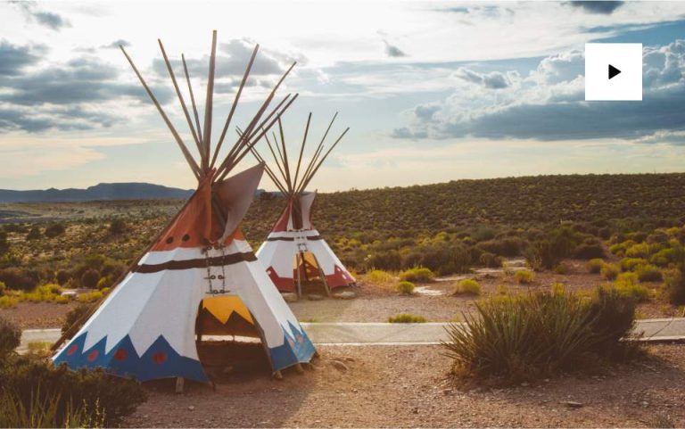 Traditional teepees in desert landscape under cloudy sky.