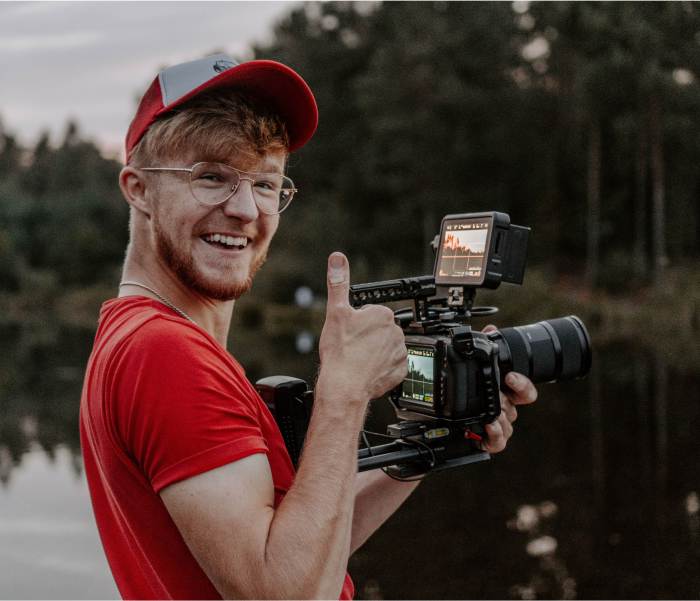 Man with camera giving thumbs up near water.