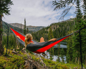 Person relaxing in hammock near forested lake.
