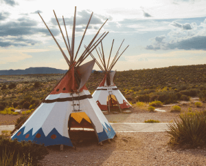 Colorful tepees in desert landscape under cloudy sky.