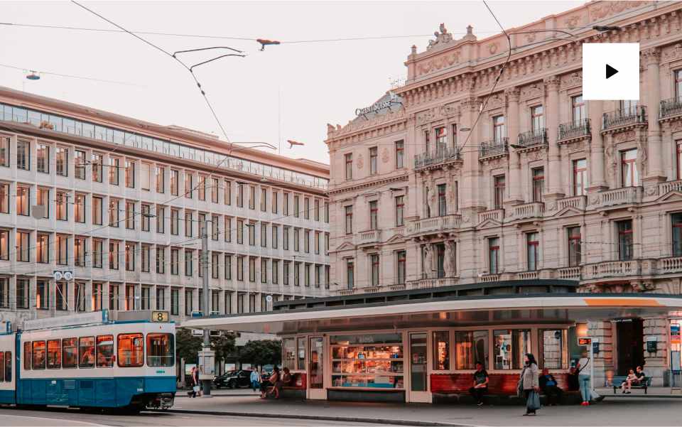 Streetcar passing city buildings at sunset.