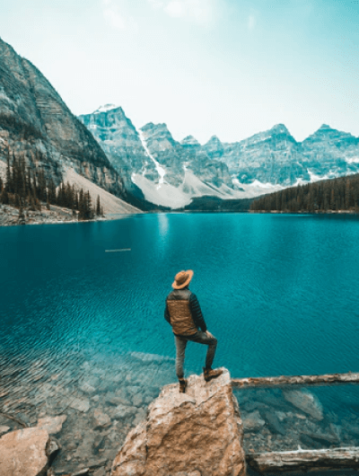 Person standing by turquoise lake, mountain view.
